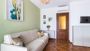 A living room with a beige sofa, a wooden door, a white cabinet, and a cactus painting on the wall. - Il Borgo Apartments B2 - Sv-d600-bove3ftb (Finale Ligure)