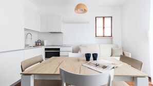 A modern kitchen with white cabinets, a wooden dining table, and a hanging light fixture. - Il Borgo Apartments B4 - Sv-d600-bove3h1b (Finale Ligure)