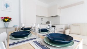 A modern dining area with a table set for four, a sofa, and a kitchen in the background. - Il Borgo Apartments B4 - Sv-d600-bove3h1b (Finale Ligure)