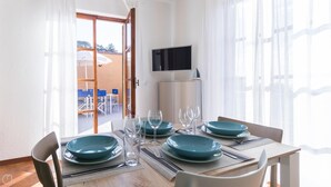 A dining area with a table set for four, a TV mounted on the wall, and a view of the outdoor seating area through the glass door. - Il Borgo Apartments B6 - Sv-d600-bove3l1b (Finale Ligure)