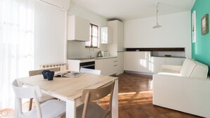 A compact kitchen with white cabinets, a dining table with chairs, and a sofa. - Il Borgo Apartments B6 - Sv-d600-bove3l1b (Finale Ligure)