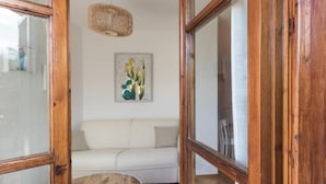A room with a wooden door, a white sofa, and a framed picture of cacti on the wall. - Il Borgo Apartments C1 - Sv-d600-navi44atc (Finale Ligure)