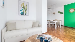 A modern living room with a white sofa, a round wooden coffee table, and a green accent wall. - Il Borgo Apartments C1 - Sv-d600-navi44atc (Finale Ligure)