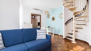 A living room with a blue sofa, a dining area with white chairs, and a spiral staircase. - Il Borgo Apartments C3 - Sv-d600-navi44c1c (Finale Ligure)