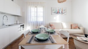 A modern kitchen with white cabinets, a stainless steel sink, and a dining area with a wooden table set for four. - Il Borgo Apartments C4 - Sv-d600-navi44d1c (Finale Ligure)