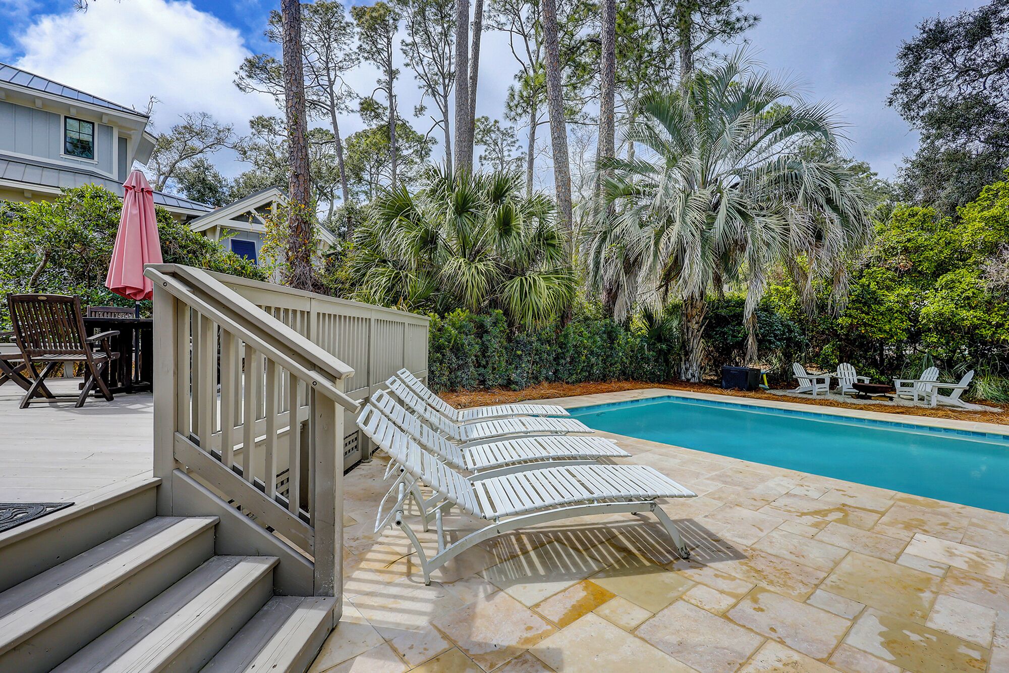 A pool area with steps leading down to the water, surrounded by lush greenery and tall trees.
