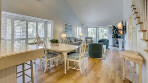 A spacious dining area with a large table and chairs, a ceiling fan, and a view of the outdoors through large windows.