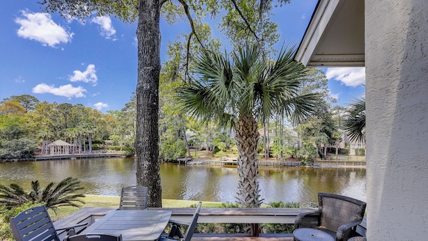 A patio with a table and chairs overlooking a lake, surrounded by trees and a gazebo.