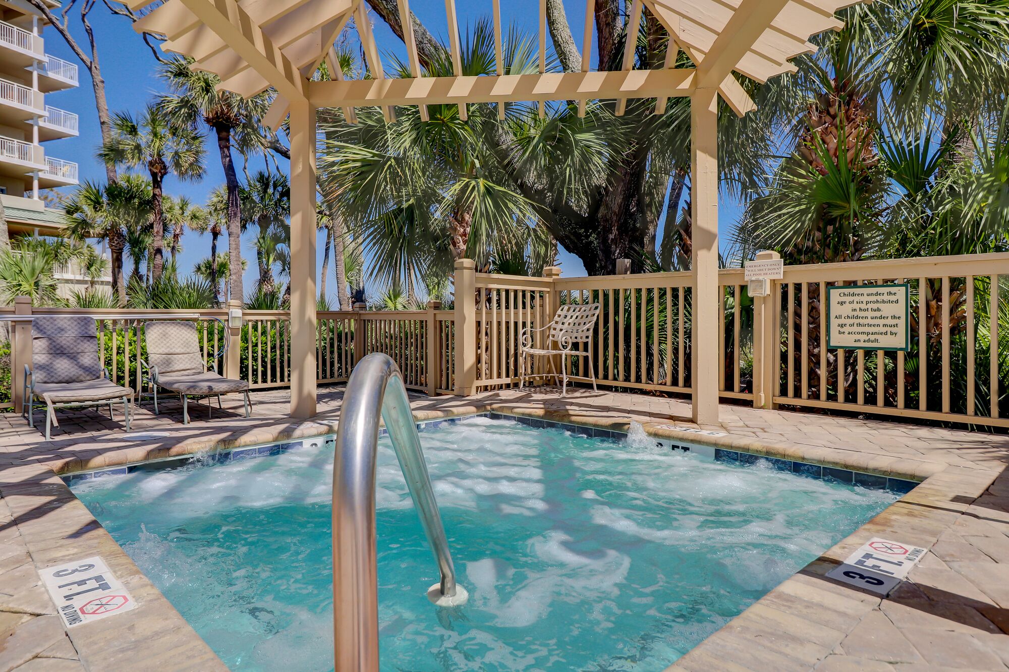 Un área de piscina con una pérgola de madera, sillas de descanso y palmeras.
