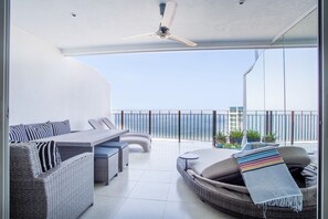 A balcony with wicker furniture, a ceiling fan, and a view of the ocean.