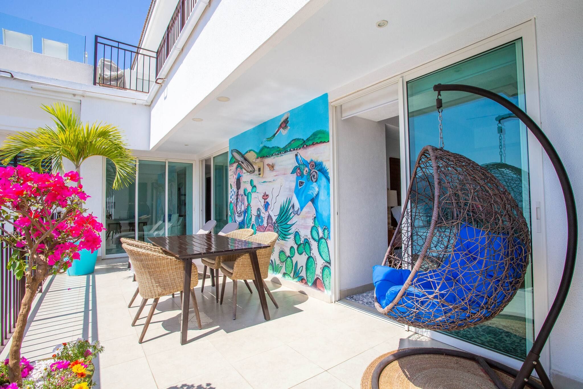 En moderne udendørs terrasse med spisebord og stole, en h ængestol og et farverigt muralmaleri på væggen.