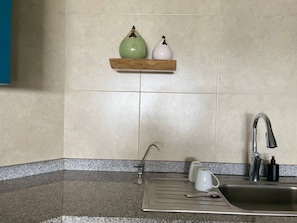 A kitchen with a stainless steel sink, a faucet, a granite countertop, and a shelf with two ceramic vases.