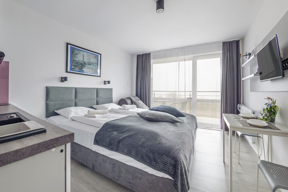 A modern hotel room with a bed, a desk, a television, and a balcony with a view.