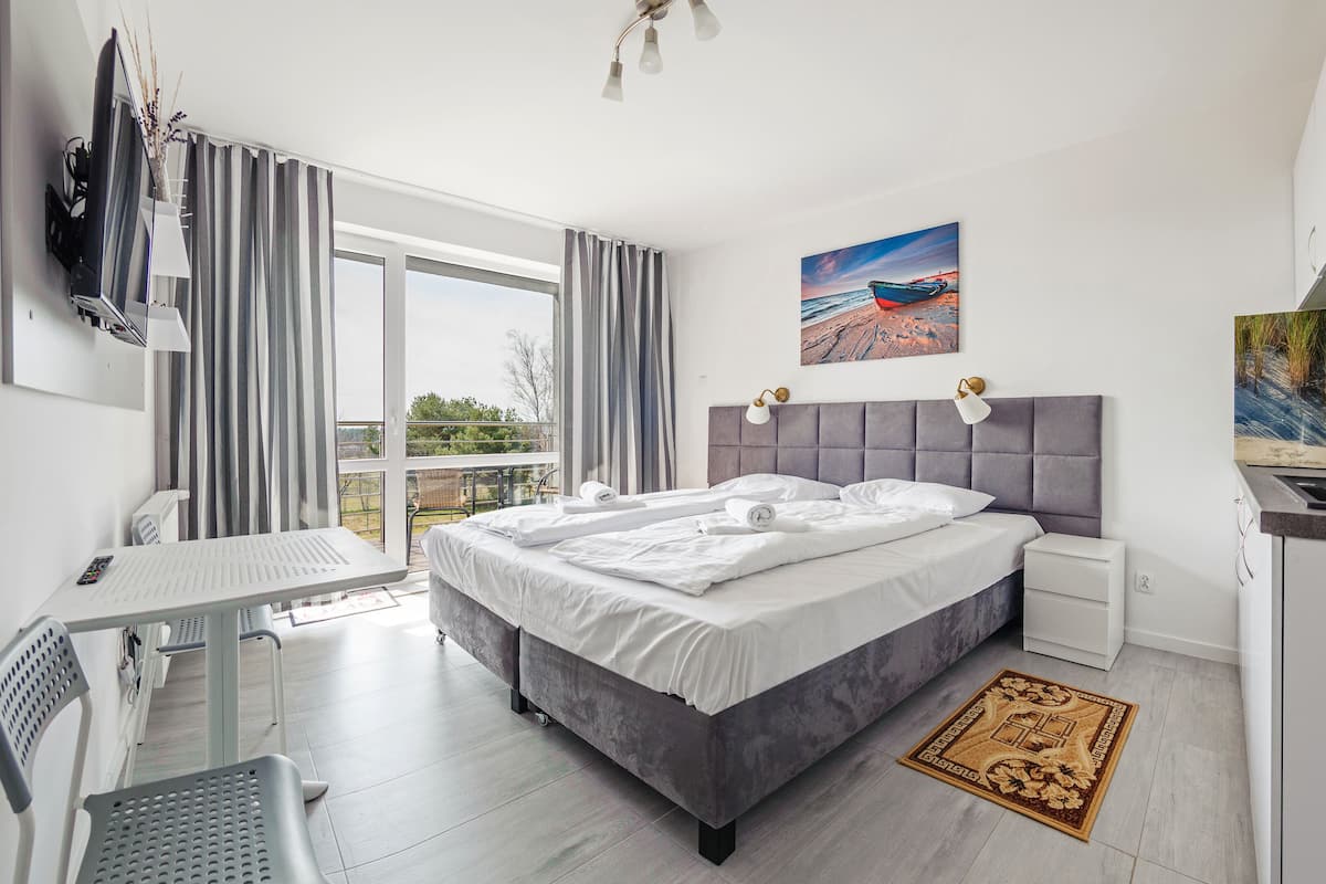 A modern bedroom with a large bed, a desk, and a view of the outdoors.