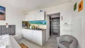 Ett modernt rum med ett litet kök, en säng och utsikt över stranden.