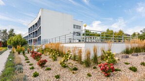 Ein modernes Gebäude mit gewölbter Fassade, Außenbereich mit Sitzgelegenheiten und einem angelegten Garten mit Kies und Blumen.