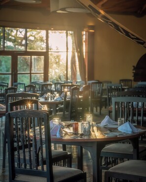 Un comedor con mesas dispuestas para dos, sillas y un centro de mesa con velas.