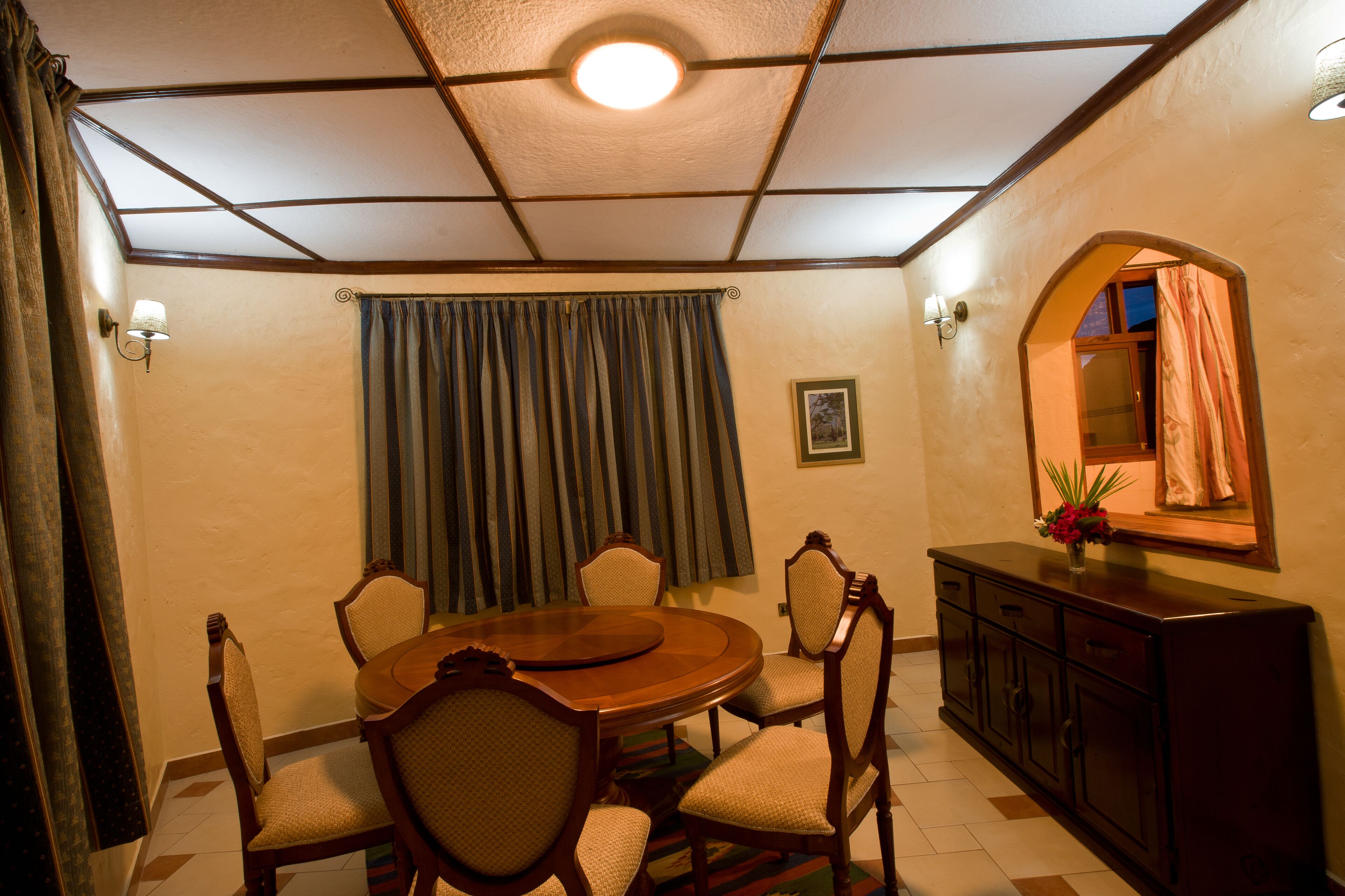 A dining area with a round wooden table, six chairs, a cabinet, and a mirror on the wall.