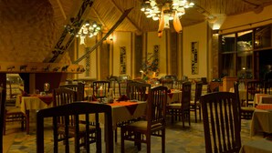 A restaurant with wooden tables and chairs, a high ceiling with hanging lights, and a patterned floor. - Amboseli Sopa Lodge (Kimana)