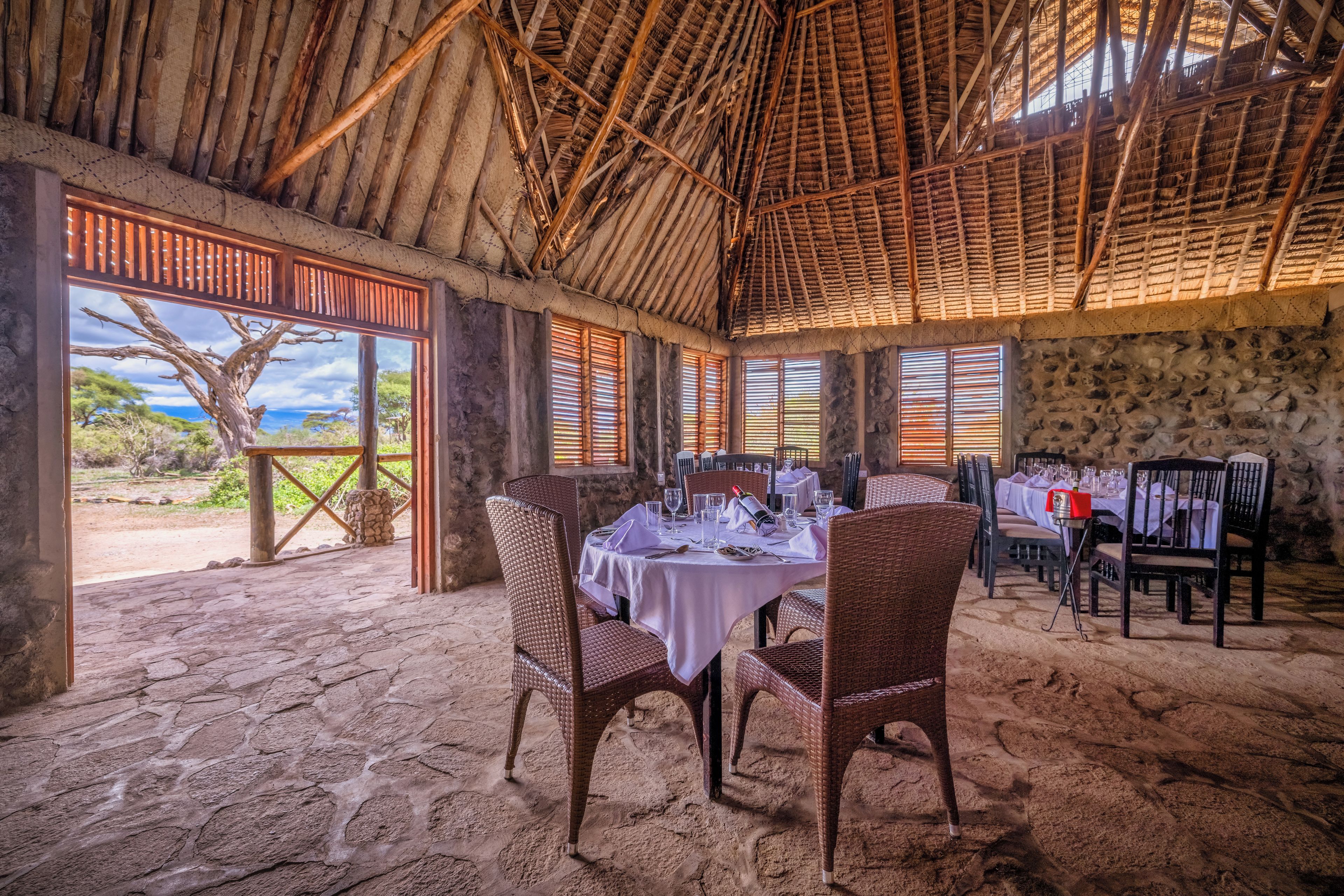 An indoor dining area with stone flooring, wicker chairs, and tables set for a meal.