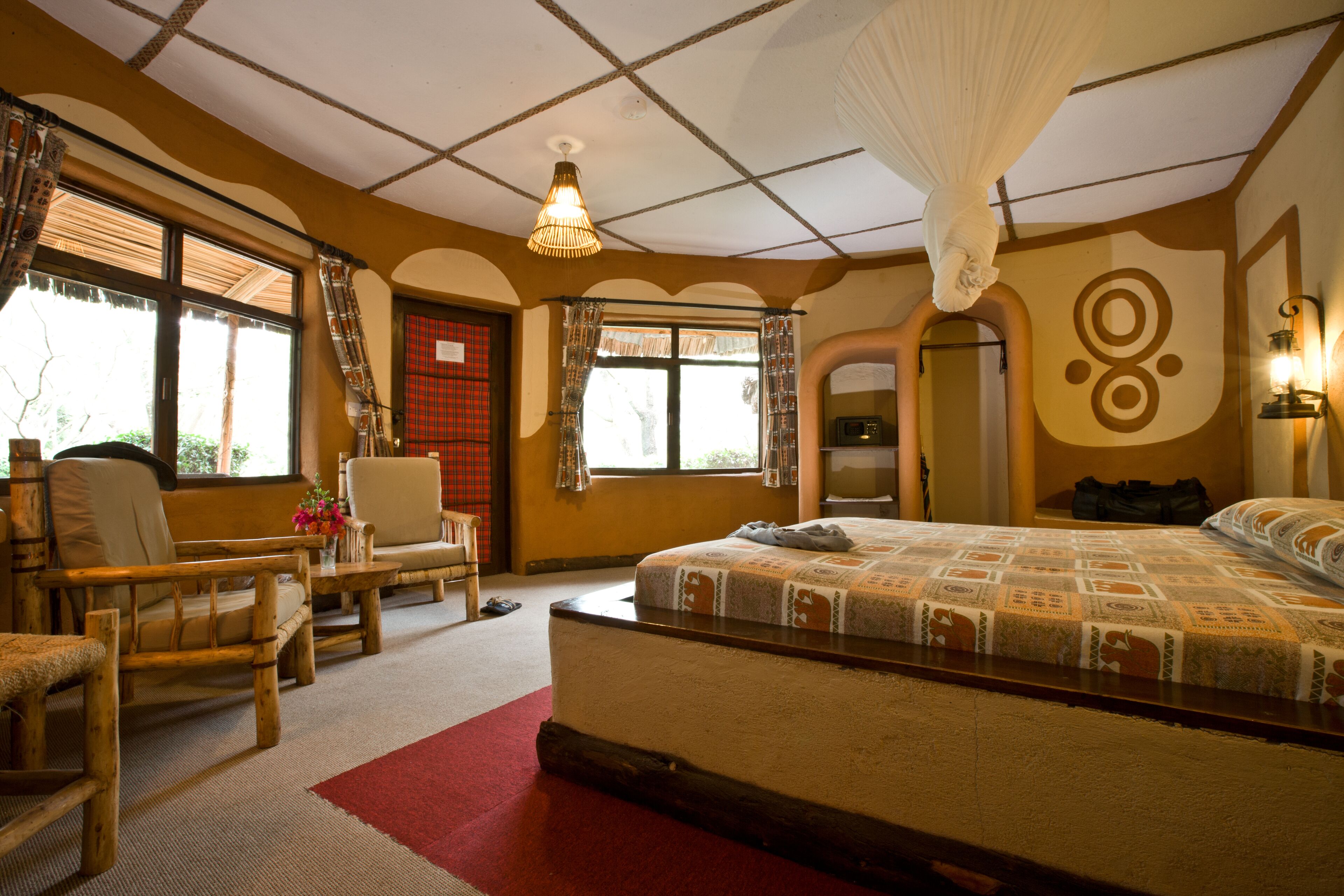 Un dormitorio con una cama grande, una zona de estar con una silla y una mesita, y una ventana con cortinas.