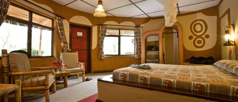 Un dormitorio con una cama grande, una zona de estar con una silla y una mesita, y una ventana con cortinas.