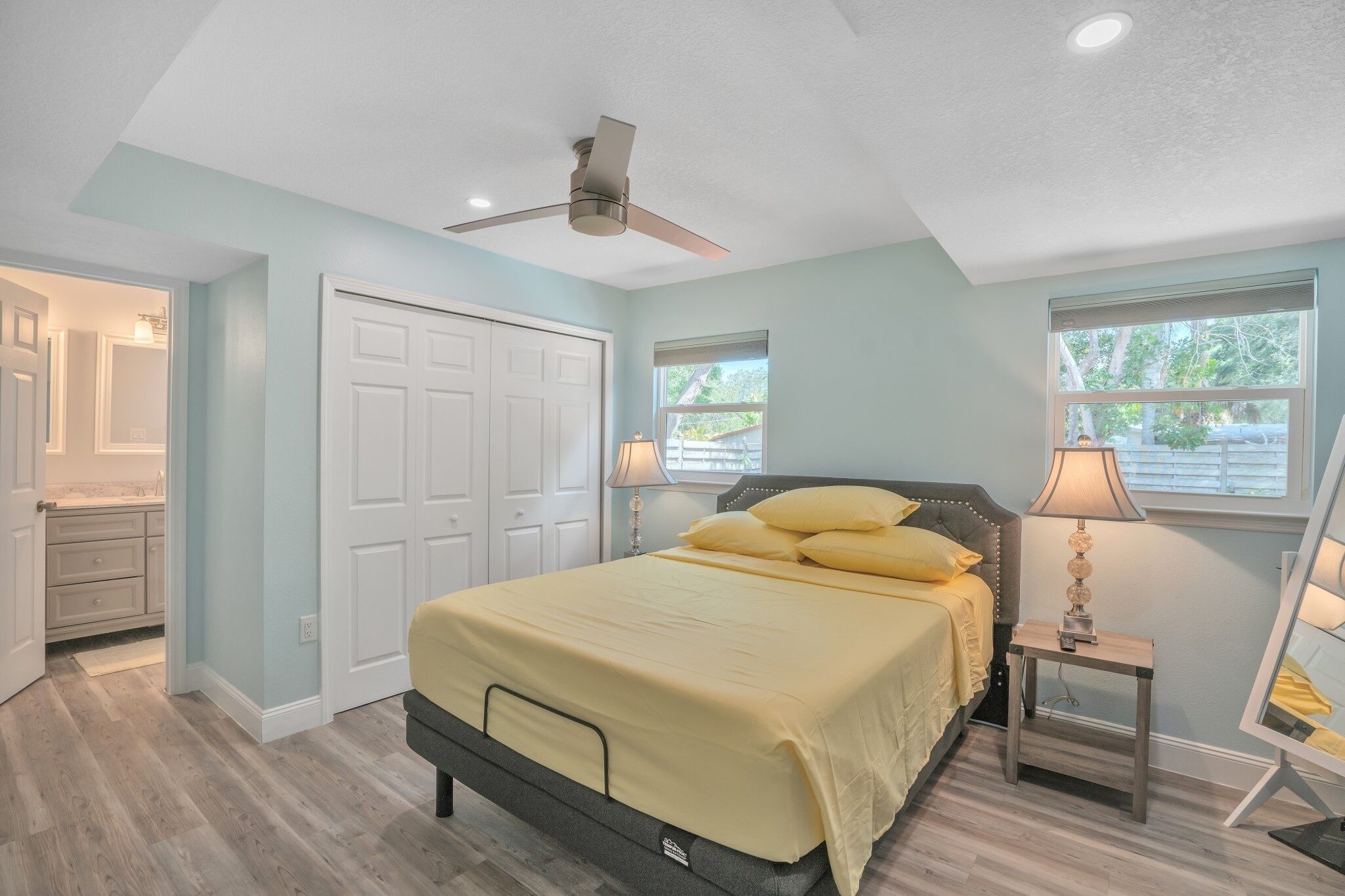 A bedroom with a bed, a ceiling fan, a nightstand with a lamp, and a window with blinds.