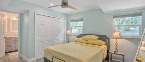 A bedroom with a bed, a ceiling fan, a nightstand with a lamp, and a window with blinds.