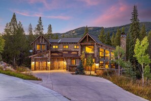 A large log cabin with multiple windows and a chimney, surrounded by trees and a mountain backdrop. - The Timber Lodge 957 7 Bedroom Home by RedAwning (Copper Mountain)
