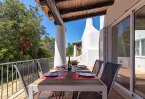 An outdoor dining area with a table set for four, surrounded by chairs, a potted plant, and a view of the surrounding landscape.