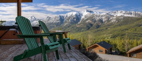 Une terrasse en bois avec des fauteuils Adirondack verts donnant sur une chaîne de montagnes.