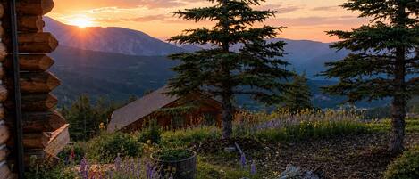 Une cabane en rondins offrant une vue sur les montagnes et un coucher de soleil.