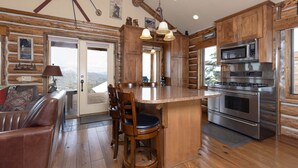 Une cuisine dotée de meubles en bois, d’un îlot central avec des tabourets de bar, d’appareils électroménagers en acier inoxydable et d’une vue sur l’extérieur, visible à travers la porte.