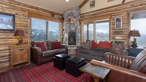 L’intérieur d’une cabane en rondins, avec une cheminée en pierre, des meubles en cuir et de grandes fenêtres donnant sur les montagnes.