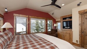 Une chambre avec un grand lit, deux fenêtres donnant sur des arbres couverts de neige, un ventilateur de plafond et un téléviseur fixé à un meuble en bois.
