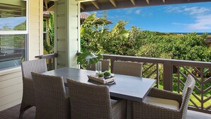 A balcony with wicker furniture and a table, overlooking a lush garden and ocean view. - Pili Mai 12L Central AC By Suite Paradise (Koloa)