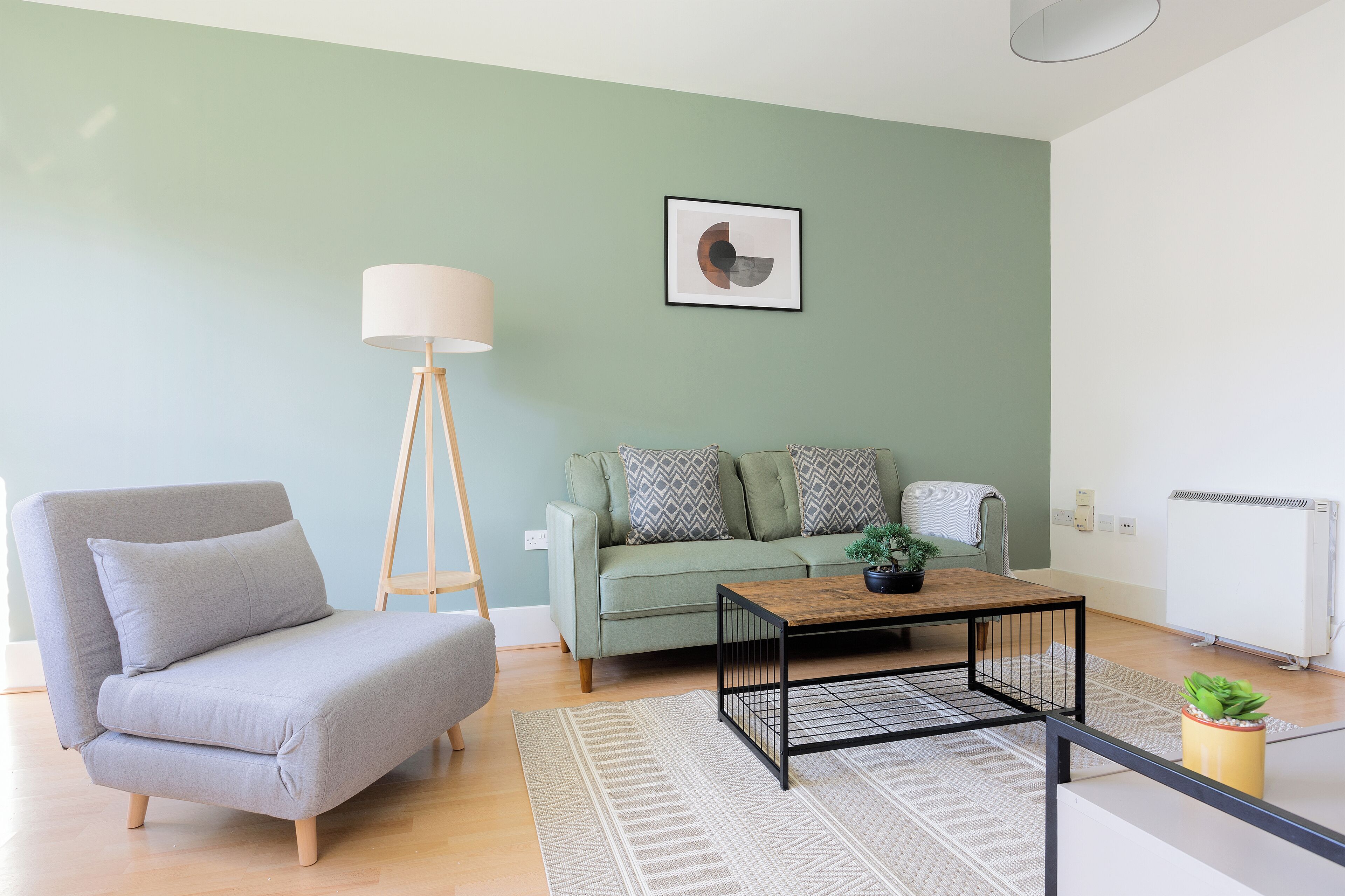 A living room with a sofa, a coffee table, a floor lamp, and a radiator.