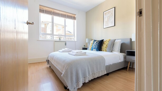 A bedroom with a bed, bedside table, and a window. - The Haggerston Flats (London)
