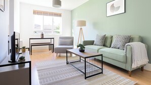 A living room with a green sofa, a coffee table, a lamp, a chair, and a TV. - The Haggerston Flats (London)