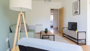 A modern living room with a sofa, a coffee table, a floor lamp, a TV on a stand, and a door leading to another room. - The Haggerston Flats (London)