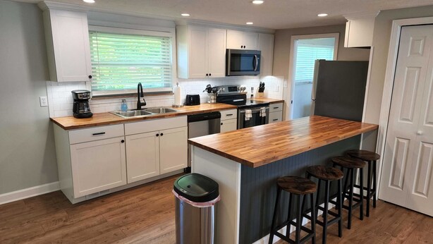 Una cocina moderna con armarios blancos, encimera de madera, microondas integrado y cafetera.