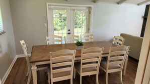 Un comedor con una mesa de madera y seis sillas, una planta pequeña en la mesa y vistas a través de una puerta con ventana.