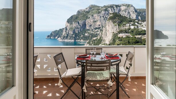 A balcony with a table set for two, overlooking a coastal cliff and sea.