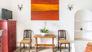 A living room with a red cabinet, two wooden chairs, a small table with a plant, and a large abstract painting on the wall.