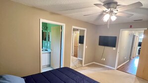 A bedroom with a bed, a ceiling fan, and a door leading to a bathroom.