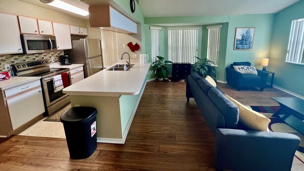 A modern kitchen with a central island, stainless steel appliances, and a dining area with a sofa and a table.