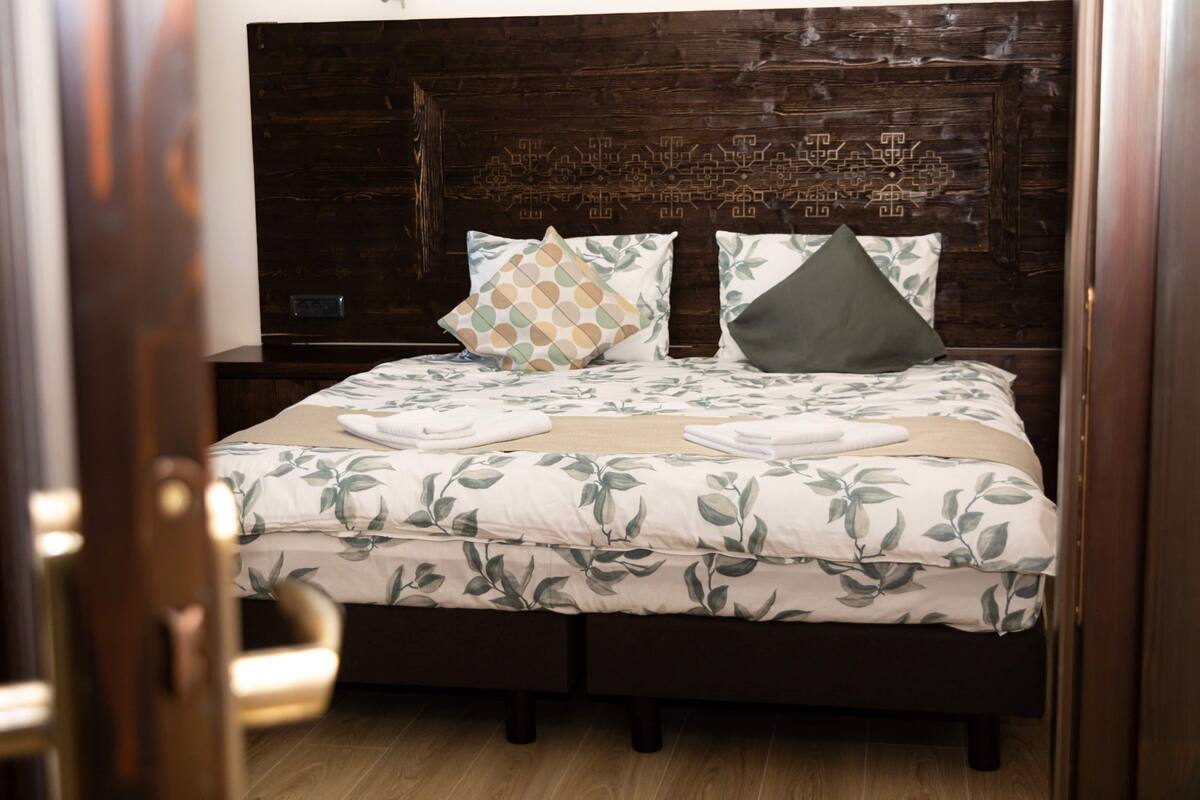A double bed with a floral bedspread, two decorative pillows, and a wooden headboard.