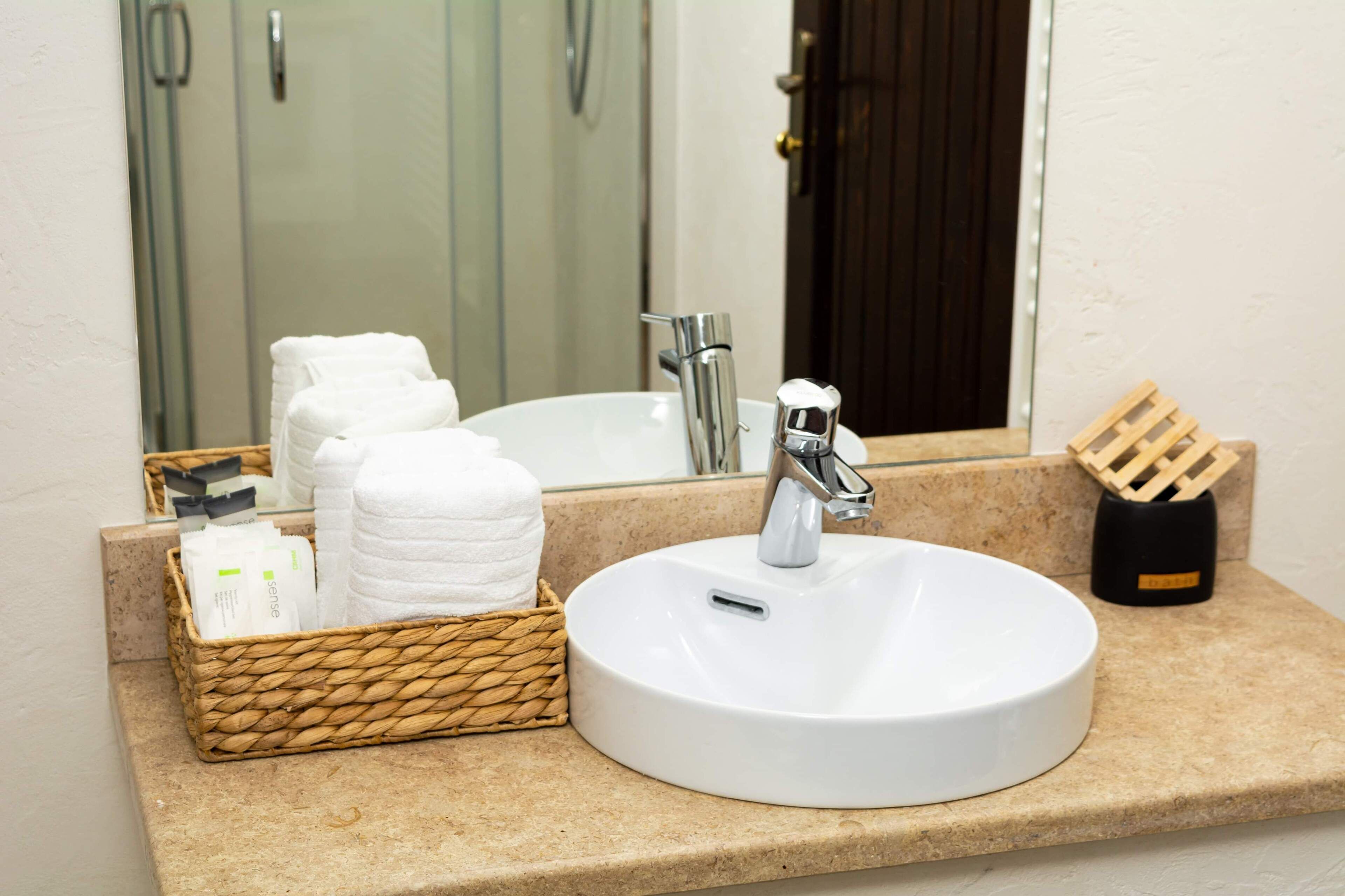 Ein Badezimmer mit weißem Waschbecken, einem Spiegel, einem Handtuchhalter und einem Tablett mit Toilettenartikeln.