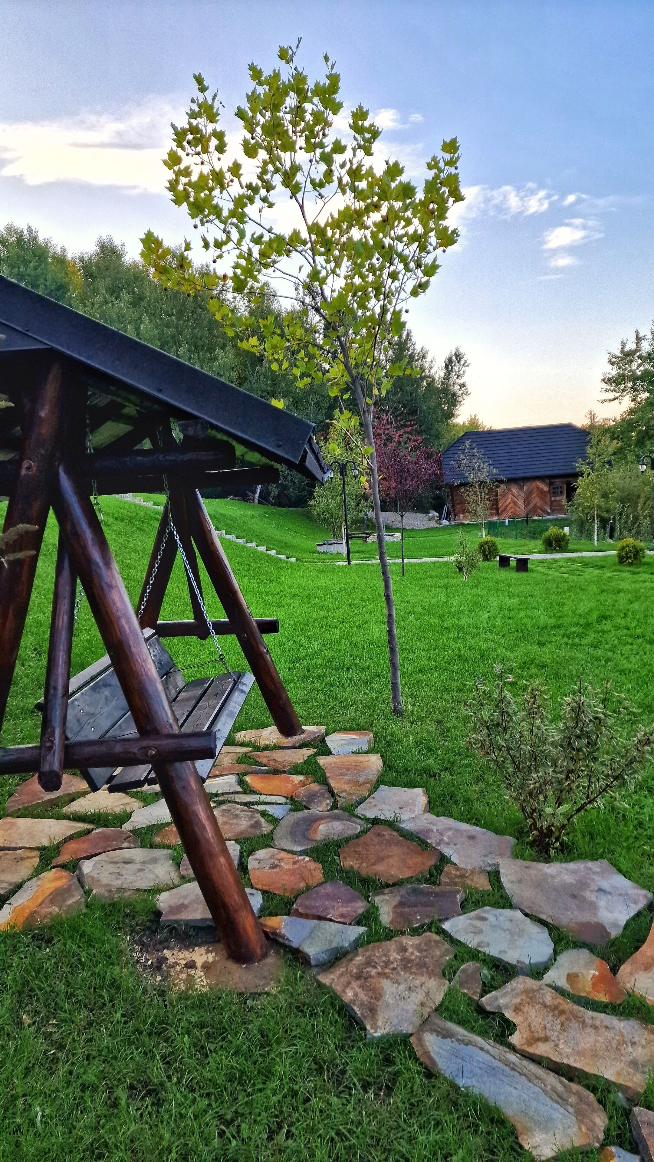 A wooden swing set in a grassy area with a stone pathway leading to a house.
