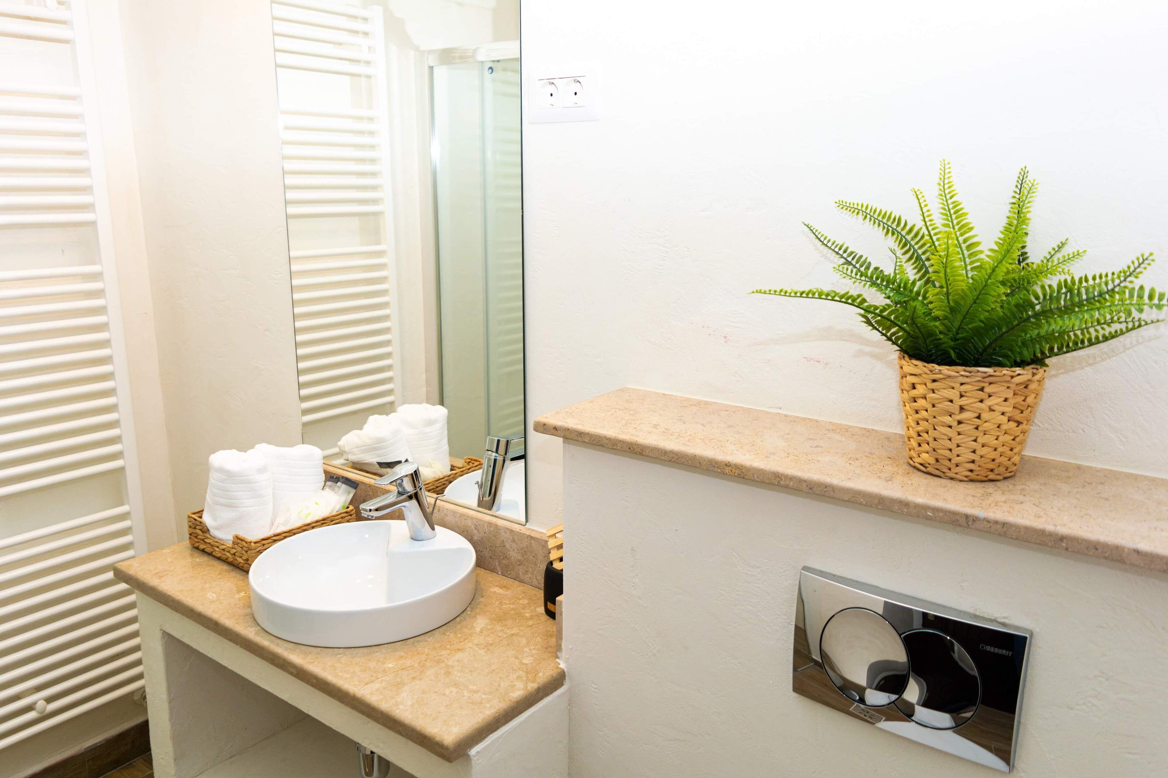 Un baño con un lavabo redondo, un espejo, un helecho en maceta y una cesta de toallas.